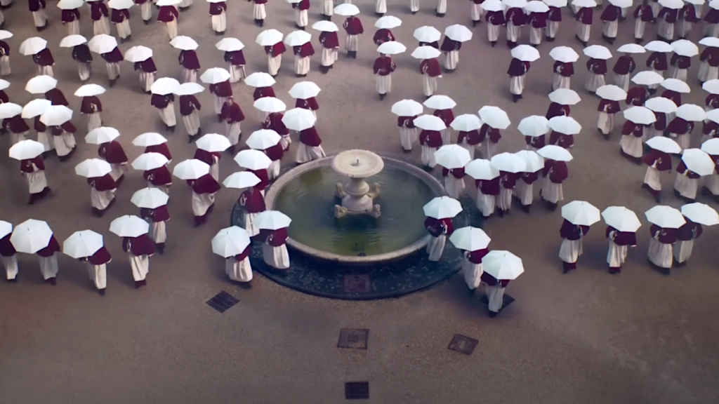 Lots of people with white umbrellas near a fountain in the movie Conclave