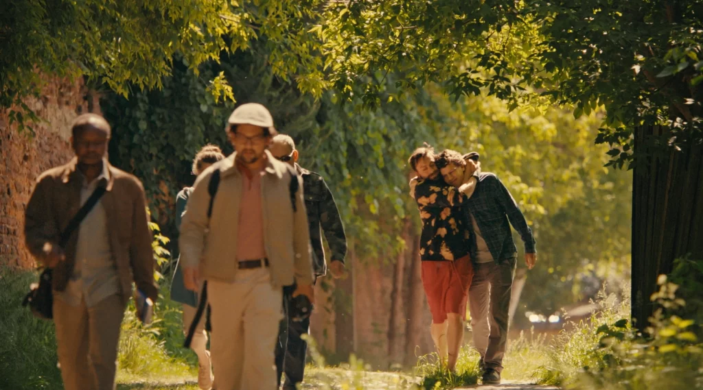 David and Jesse are walking a forest path together. Benji has his arm around David.