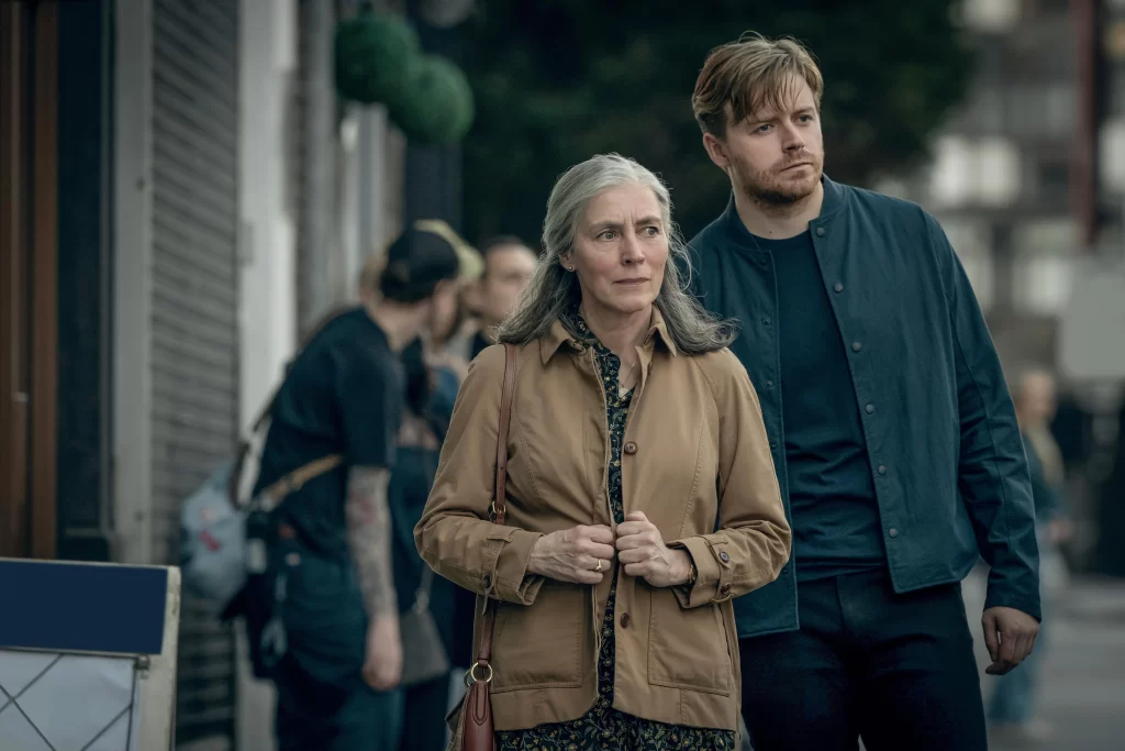 An older woman and a younger man walking down the street, they look across the street with concerned expressions